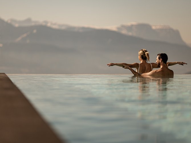 Welkom in Gitschberg Jochtal! Man en vrouw baden in een infinity pool. Op de achtergrond een bergachtig landschap.