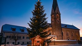 Tearna Advent Weihnachtsbaum mit Krippe vor Kirche bei Dämmerung im verschneiten Dorf