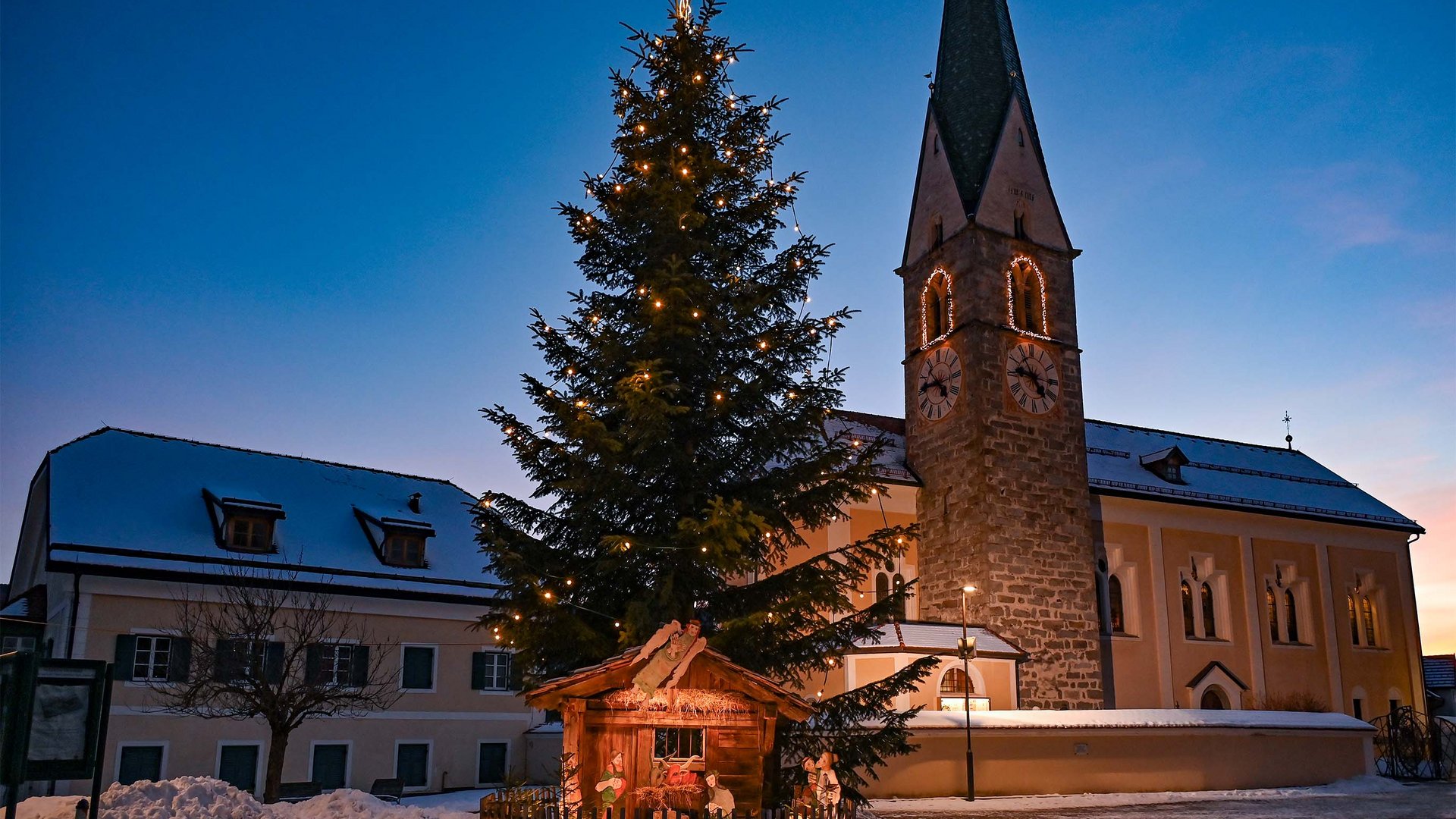 Tearna Advent Weihnachtsbaum mit Krippe vor Kirche bei Dämmerung im verschneiten Dorf