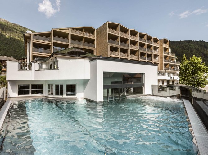 Willkommen in der Ferienregion Gitschberg Jochtal! Außenpool mit Blick auf modernes Hotelgebäude und Berge