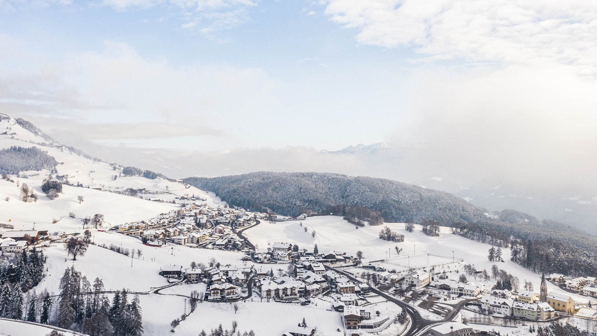 Terenten in het Pustertal Besneeuwd dorp in een dal met beboste heuvels onder een bewolkte lucht
