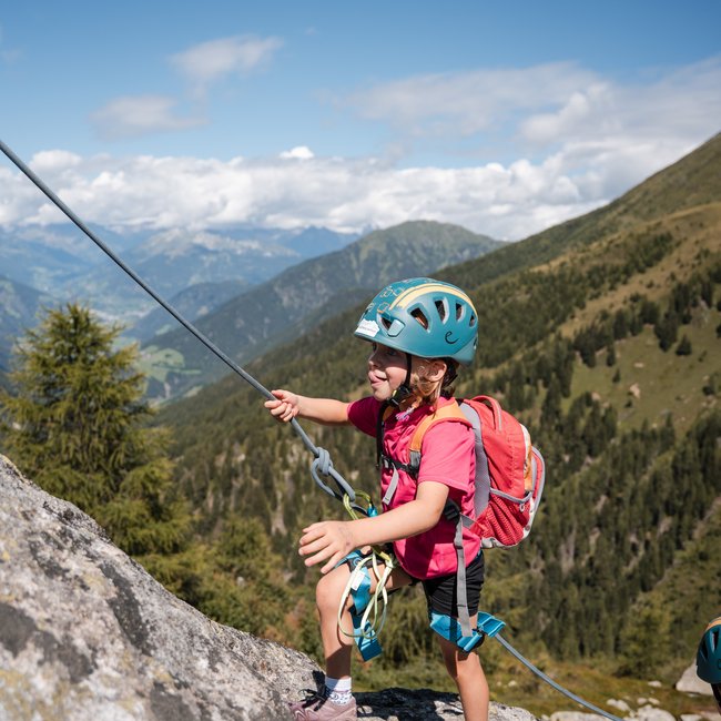 Euer Familienurlaub in Südtirol Kleines Kind mit Helm klettert gesichert einen Felsen in den Bergen hinauf